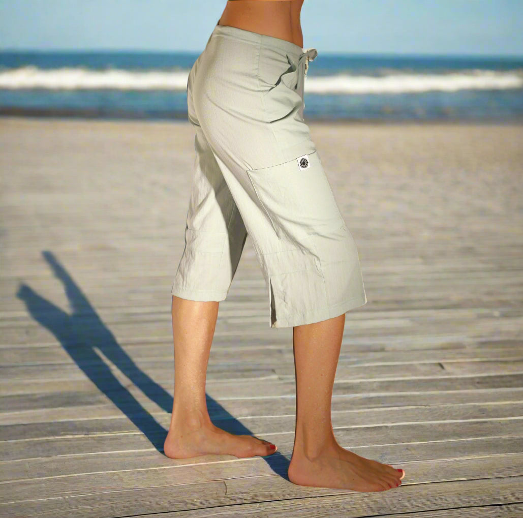 Woman standing on a beach wearing the eco-friendly Seafoam Bliss Pant in sustainable Tencel fabric — short yoga pants with 15.5" inseam with slits in the back and drawstring waist