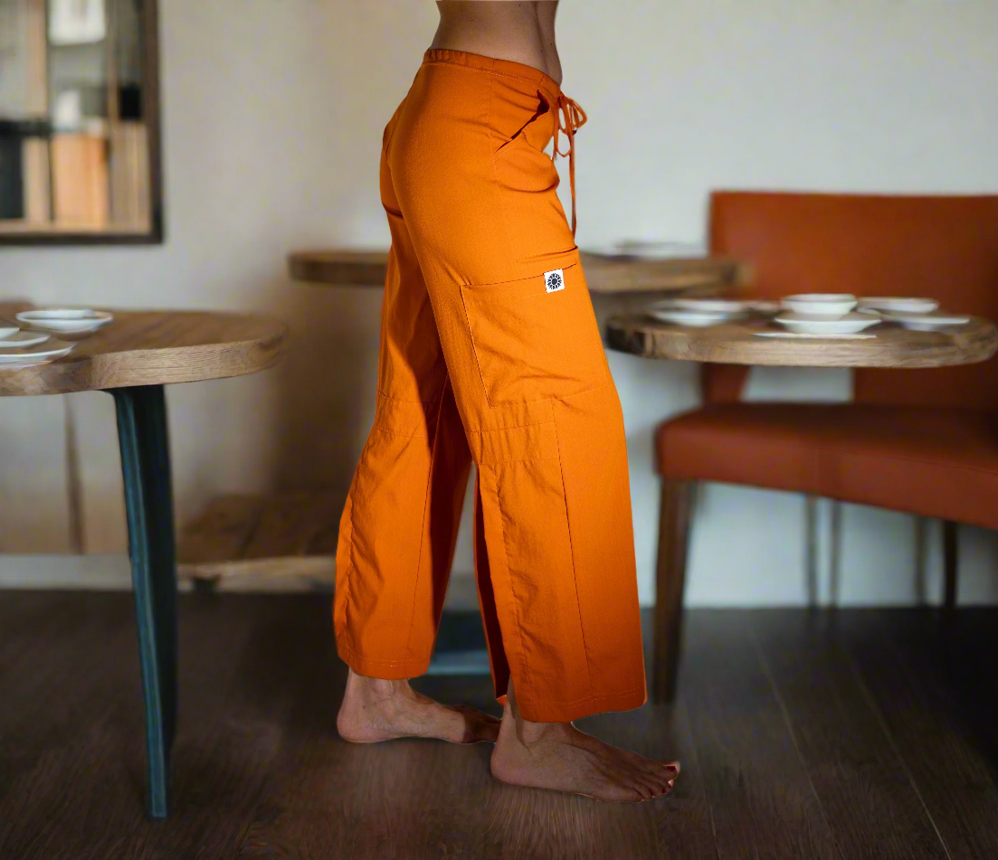 Women's eco-friendly Paprika orange Freedom Pant in sustainable Tencel fabric — wide-leg yoga pants with drawstring waist and cargo pockets showing the side view with logo on the pocket